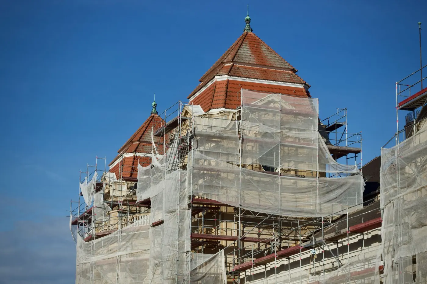 Historisches Gebäude mit Ziegeldach hinter Baugerüst und Schutznetzen
